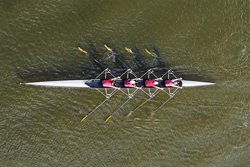 An above shot of four people rowing a boat on water.