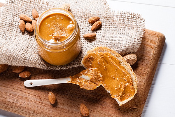 almond butter in a jar next to it spread on a piece of bread