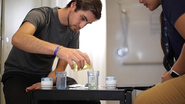 Young white male pouring urine into a sample collection cup in view of doping control officer.