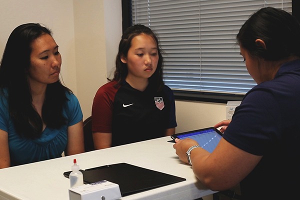 Young asian female athlete with mother talking to a doping control officer at a table.