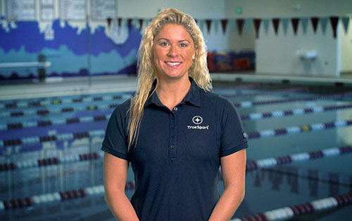 Elizabeth Beisel standing in front of a pool wearing a TrueSport polo shirt.