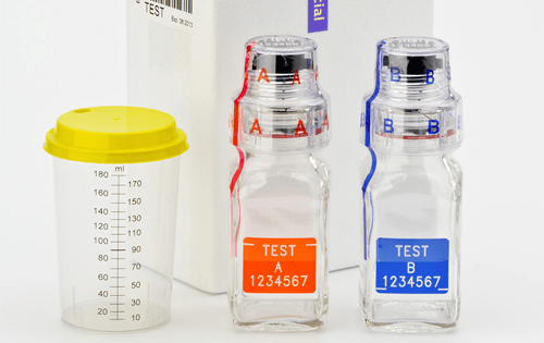 Berlinger sample bottles and urine cup against a white background.