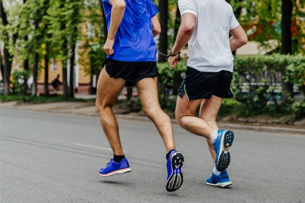 Two male athletes running connected by a chain as one athlete is blind.