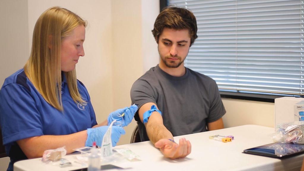 Male athlete getting a bood draw from a female blood collection officer.