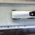 white bobsled with two athletes going down a luge track