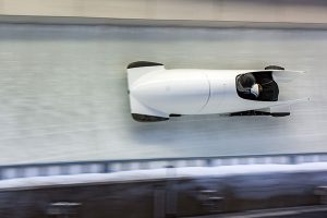 white bobsled with two athletes going down a luge track