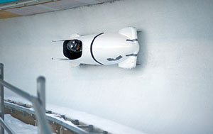 A white two person bobsled going down a track.