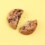 A broken chocolate chip cookie on a yellow background.