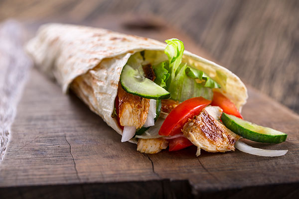 Chicken wrap with vegetables on a wood table.