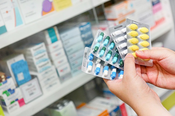 hands of person in pharmacy holding multiple blister packs of medication.