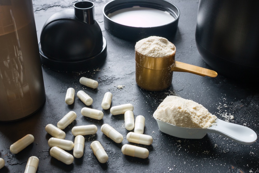 White supplement pills on a dark table next to powered supplements in containers.