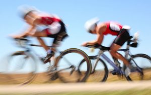 two cycling athletes slightly blurred as they race past fast