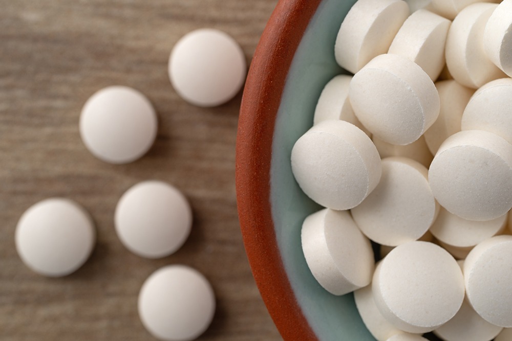 Small white DHEA tablets in bowl and on table.