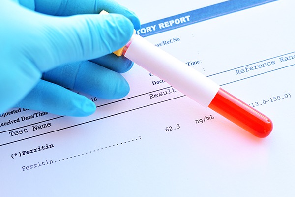 Gloved hand holding vial of blood over ferritin test results.