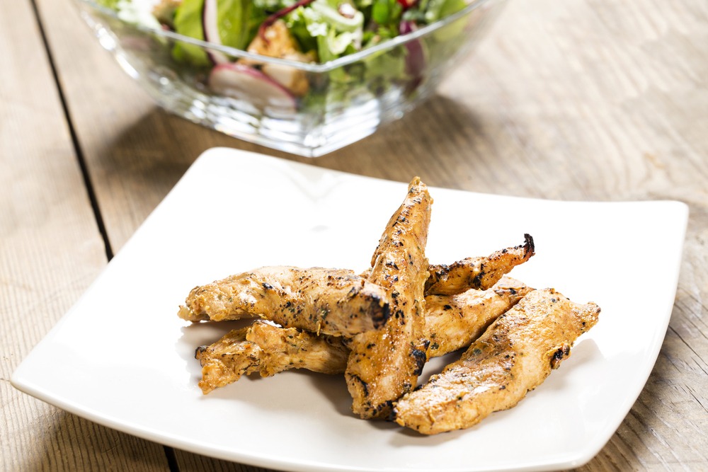 Grilled chicken strips next to a salad.