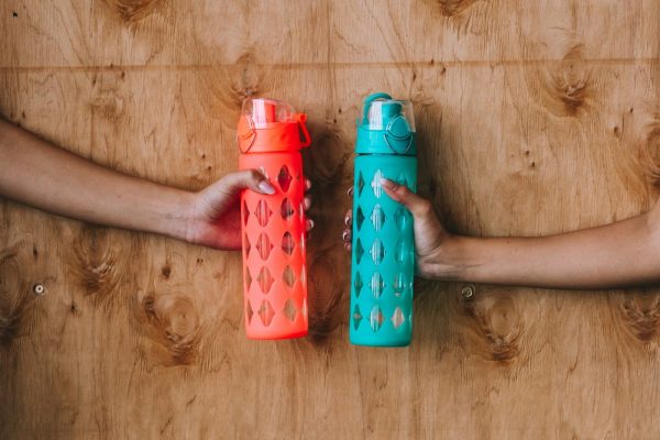 Two hands holding different colored reusable sport water bottles.