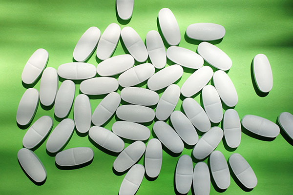 pile of white oval tablet pills on a green background with shadows overlaid
