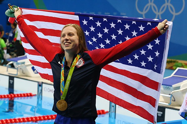 Lilly King holding the United States Flag while at the Olympics with a medal around her neck.