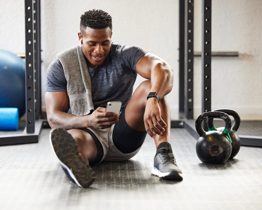Man sitting in gym looknig at smart phone.