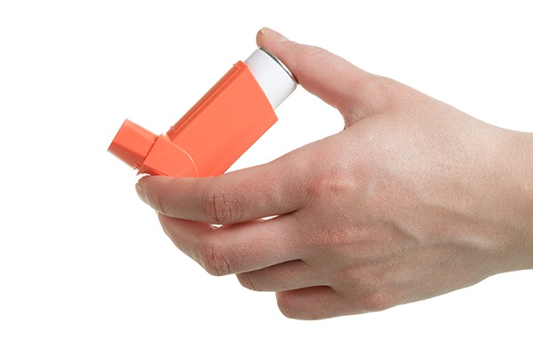 Hand holding an orange inhaler on a white background.