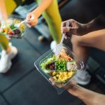 Man and woman eating salad with beans and rice in a gym.