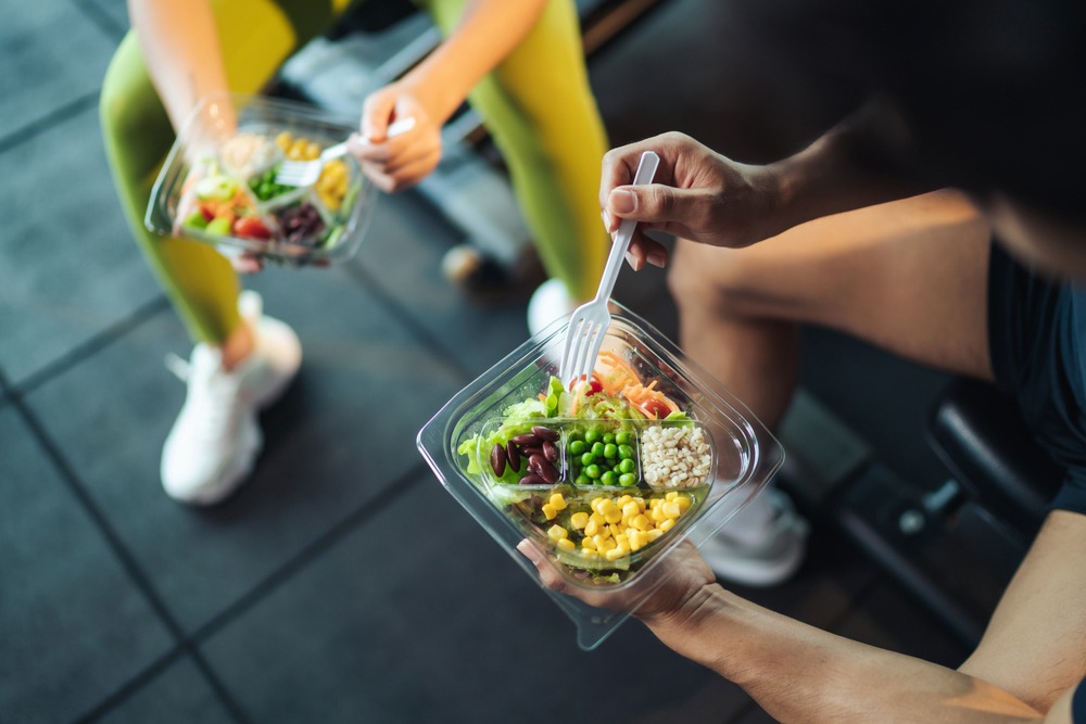 Man and woman eating salad with beans and rice in a gym.