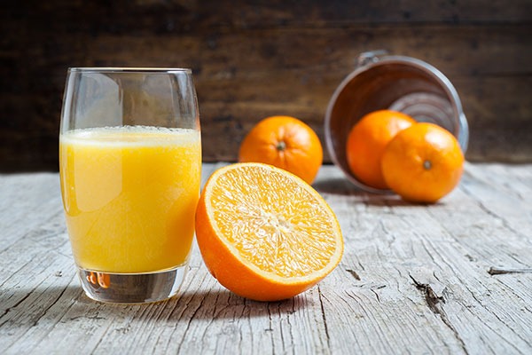 A glass of orange juice next to half an orange.