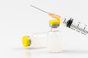 Two vials of cloudy liquid with yellow tops with a syringe sitting on top.