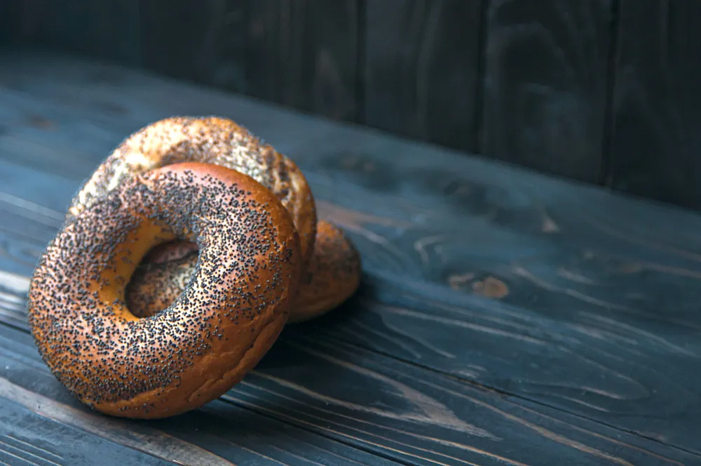 Two poppy seed bagels on wood table.