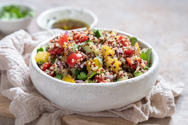 Quinoa salad with vegetables in a white bowl.