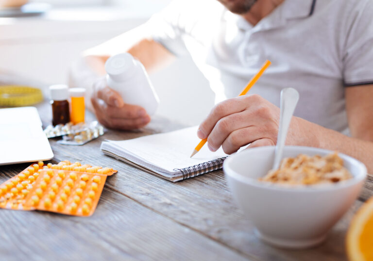 man looking at pill bottle while writing on pad of paper