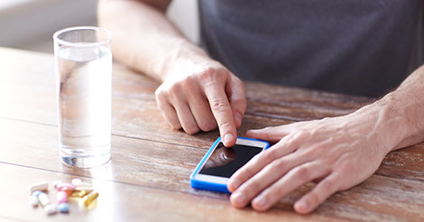 pills and glass of water on table while person scrolls through phone