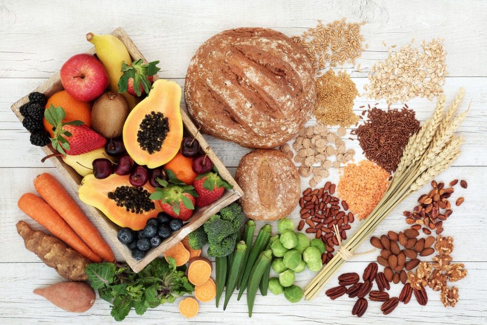 High fiber foods against a white background, including fruits, vegetables, breads, and legumes.