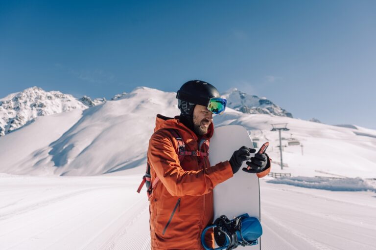 Male snowboarded on mountain looking at phone while holding snowboard.