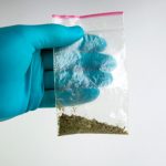 Gloved hand holding a bag of synthetic cannabinoids.