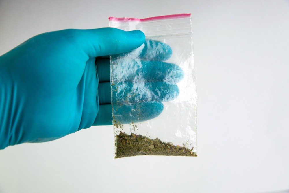 Gloved hand holding a bag of synthetic cannabinoids.