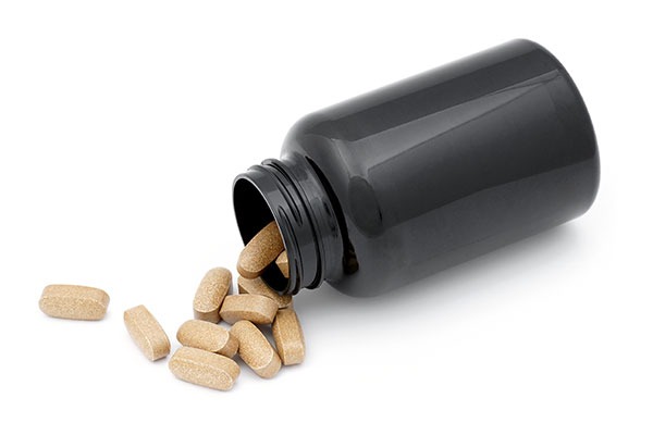 black pill bottle with natural looking pills spilling out