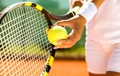 A hand holding a tennis ball against a tennis racket.