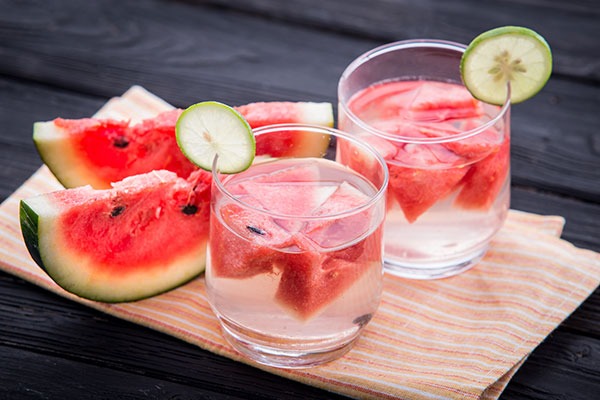 sliced watermelon on a wooden board next to two glasses of water with watermelon floating within