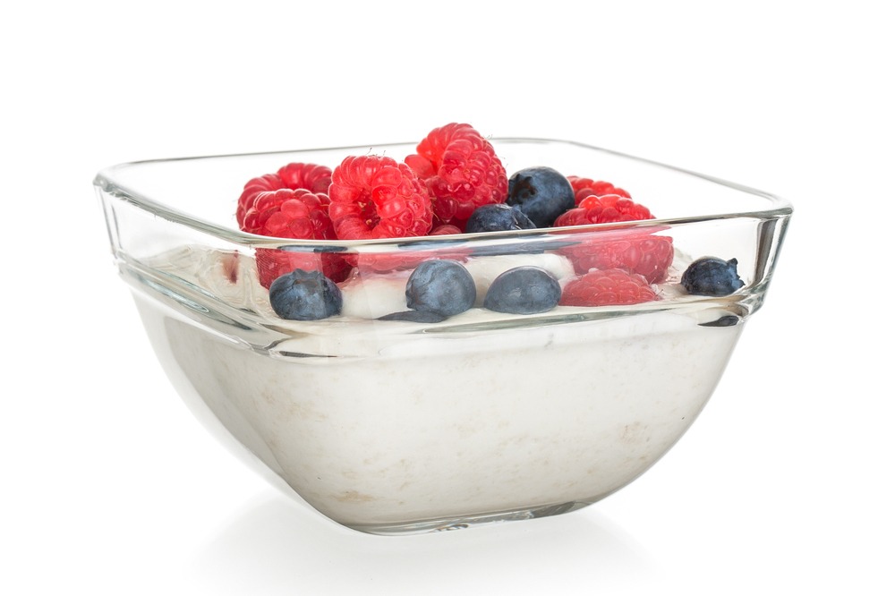 Glass bowl of white yogurt with berries on top.