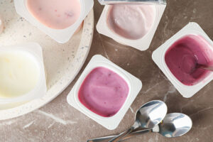 Store bought yogurts of different flavors next to spoons.